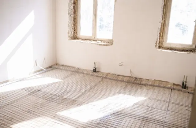 Unfinished room under renovation with two large windows, white walls, and a steel reinforcement grid on the floor for concrete.