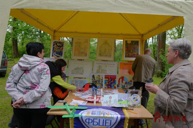Outdoor art stall under a yellow canopy, framed drawings and colorful posters on display while people browse.