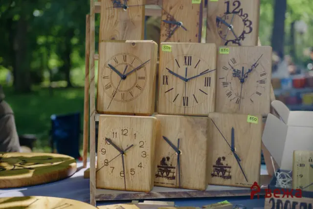 Stack of wooden clocks with Roman numerals on display at an outdoor market stall.