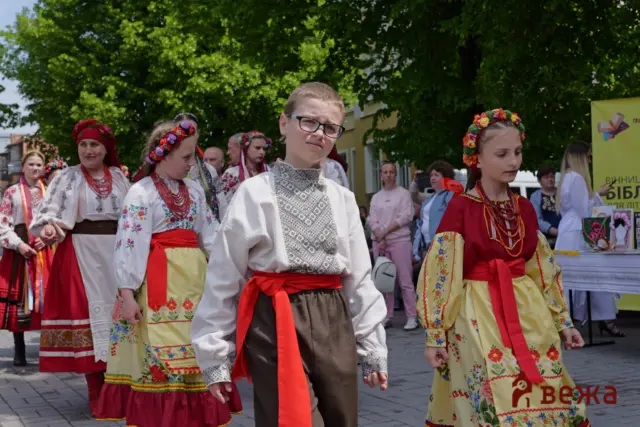 Group of people in traditional Ukrainian folk costumes dancing at an outdoor festival with green trees in the background.