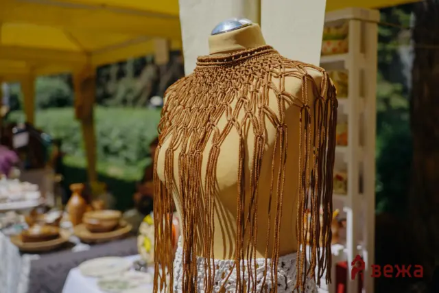Mannequin wearing a brown macrame fringe garment at an outdoor market stall