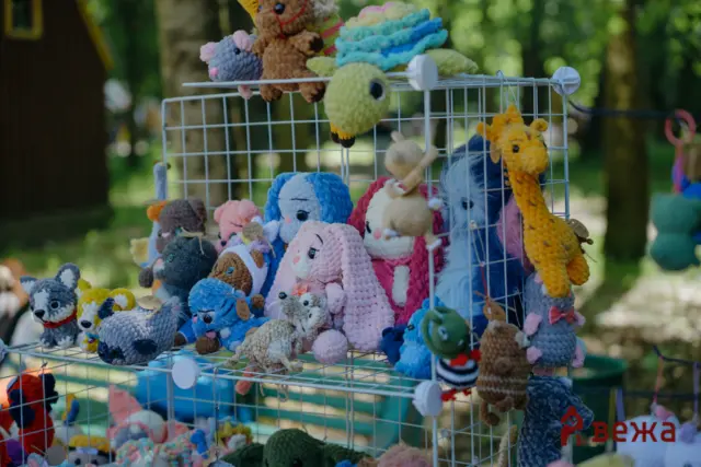 Colorful crocheted stuffed animals hanging on a market stall wire rack outdoors.