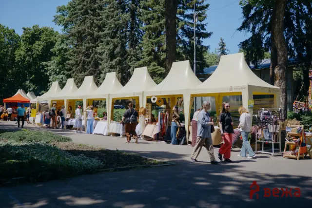 Outdoor market with cream-colored tents and shoppers browsing stalls on a sunny day.