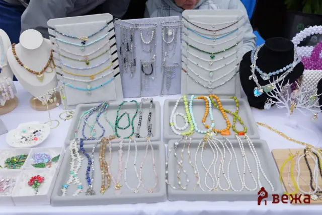 Colorful beaded necklaces and bracelets arranged on gray display boards at a market jewelry stall.