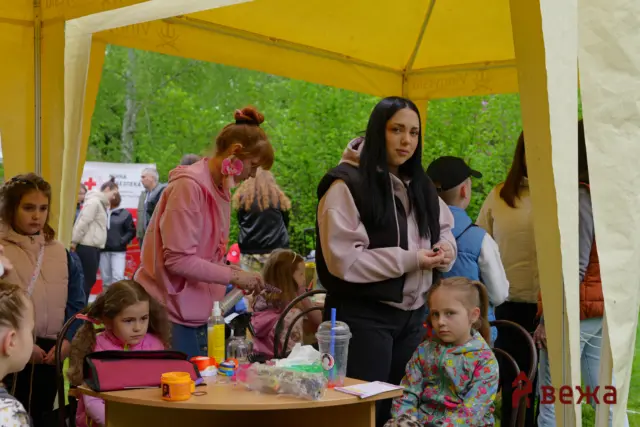 Children at an outdoor craft activity under a yellow tent, with tables, supplies, and kids working together.