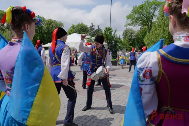 Group of performers in bright Ukrainian folk costumes dancing and playing drums at an outdoor festival on a sunny day.