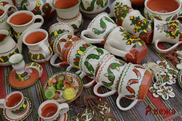 Crowded display of white hand-painted ceramic cups and bowls with red interiors and bright floral patterns on a striped cloth.