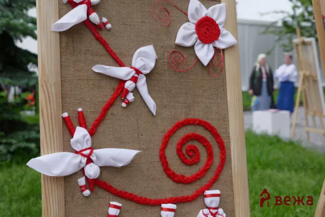 Decorative burlap board with white fabric bows and red rope swirls tied to a wooden frame, outdoors.