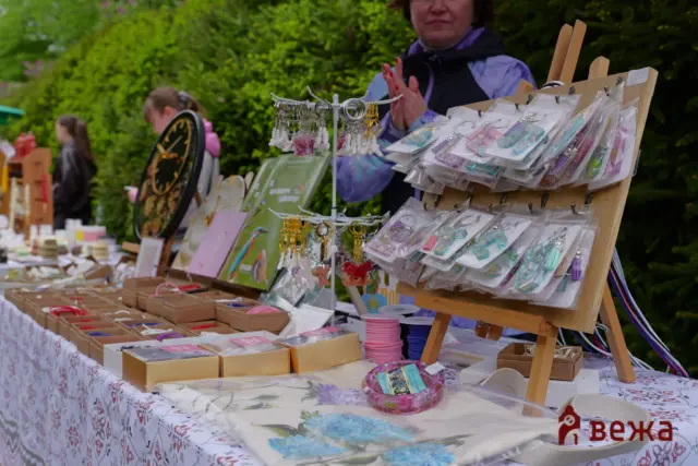Outdoor market stall selling earrings, keychains and small crafts on a table with a patterned cloth.