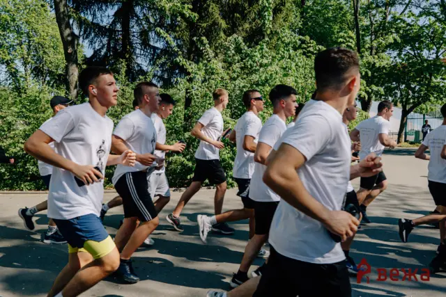 A group of runners in white shirts jogging along a sunny street with trees in the background.