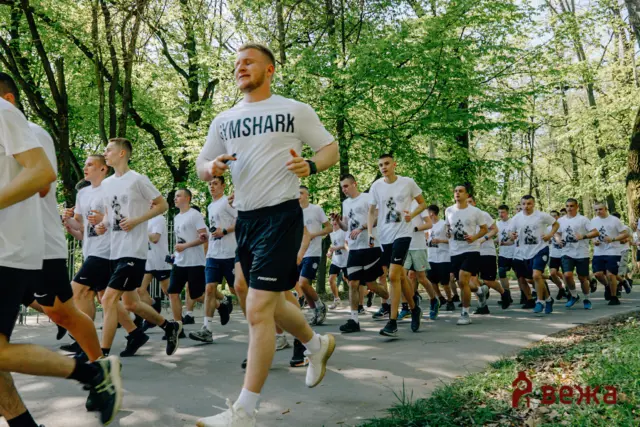 Group of runners in white shirts sprint along a tree-lined park path during a race.