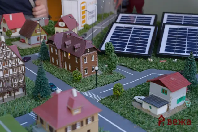Miniature town with red-roof houses, winding roads, trees, and solar panels in the background.