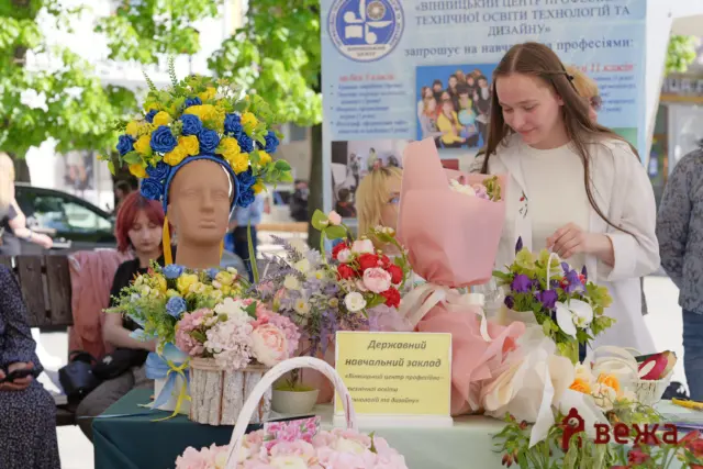 Bust mannequin wearing a blue-and-yellow flower crown among colorful bouquets at an outdoor market stall