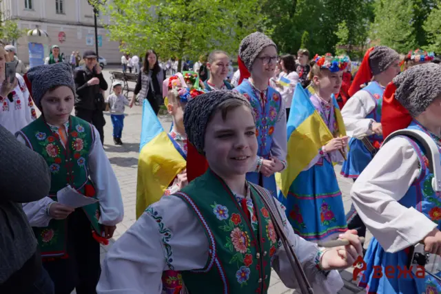 Group of people in colorful Ukrainian folk costumes marching in a parade, waving blue and yellow flags on a sunny street.