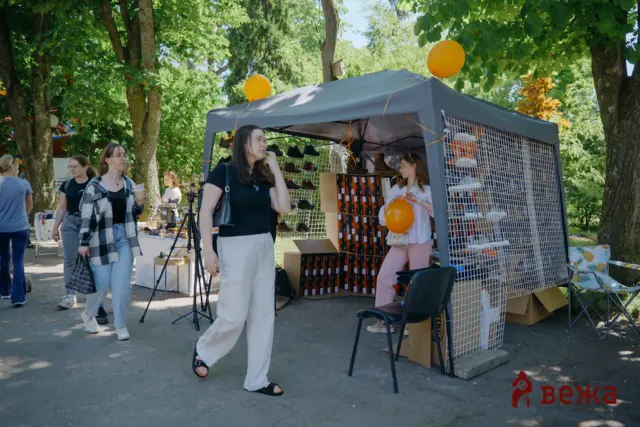 Outdoor market stall under trees with shoe display and people browsing; orange balloons tied to the canopy.