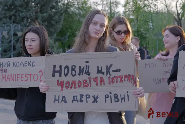 Group of young women protestors holding large cardboard signs with handwritten Ukrainian text outdoors in a park.