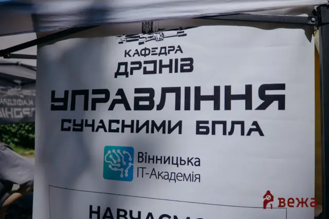 A printed sign in Ukrainian with the heading 'КАФЕДРА ДРОНІВ' and large bold text beneath, likely a tech event banner for IT Academy/Vinnytsia IT-Academia shown outdoors under a canopy.