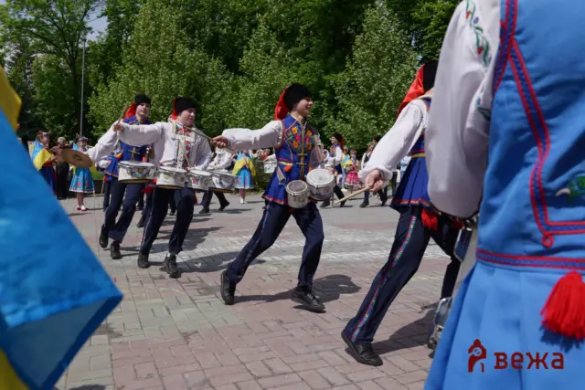 Group of drummers in traditional Ukrainian attire marching outdoors, playing snare drums.