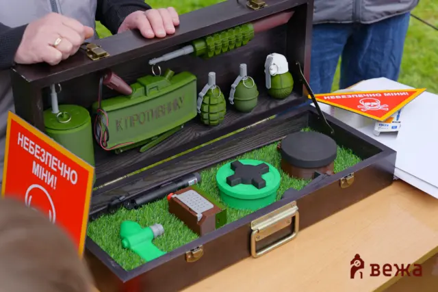 Display box with green toy grenades, signs in Cyrillic and a faux safety briefing setup for a demo kit.