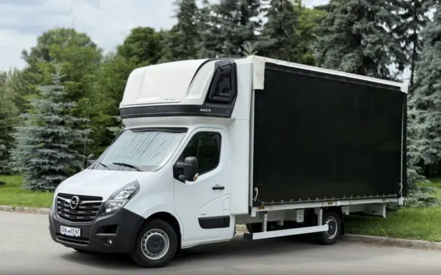 White box truck with a tall black cargo area parked on a paved road, with trees in the background.