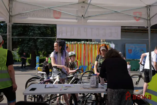 Group of people at an outdoor bike event under a white canopy, with bikes at a registration table and papers in view.