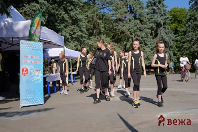 Group of young female athletes in black and neon outfits walking outdoors at a sports event near tents and banners.
