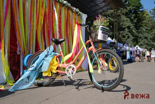 Colorful ribbons decorate a bike with a flower-filled basket at a sunny outdoor festival event.
