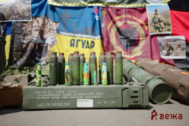 Row of green artillery shells on a military crate, with war posters and flags in the background.