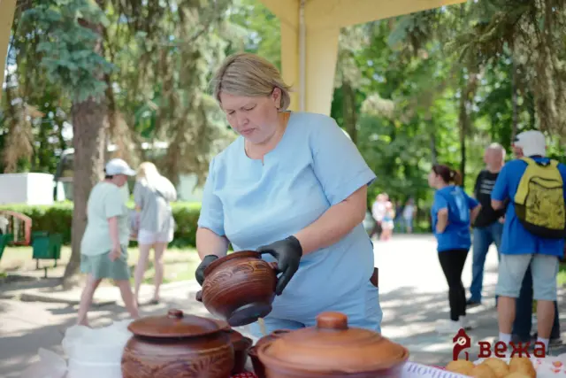 Woman in a light blue shirt wearing gloves arranges brown pottery pots at an outdoor market stall.