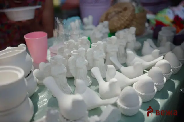Table displays many small white ceramic figurines and bowls, with a pink cup in the background at a market stall.