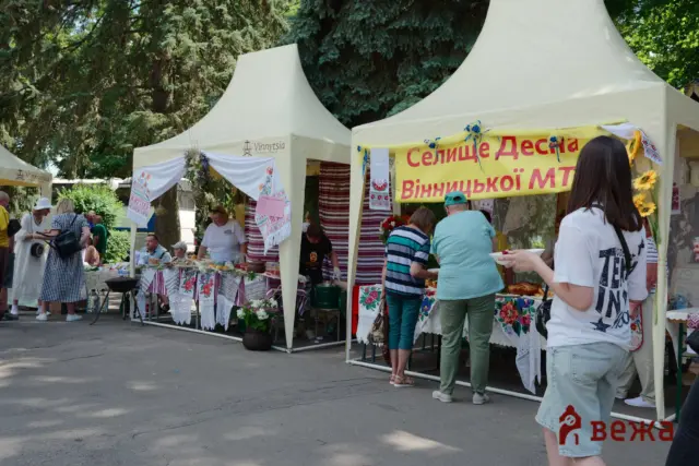 Outdoor market stalls with embroidered textiles and flower decorations, people browsing a variety of handmade goods under white tents.