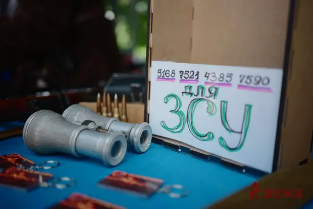 Close-up of spray paint cans on a blue work surface beside a cardboard sign with large green graffiti text and numbers.