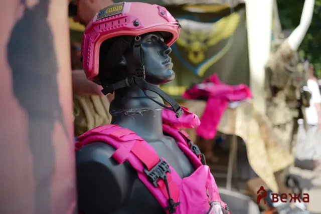 Gray mannequin wearing bright pink protective gear: helmet and jacket with black straps, outdoor blurred background, gear display image.