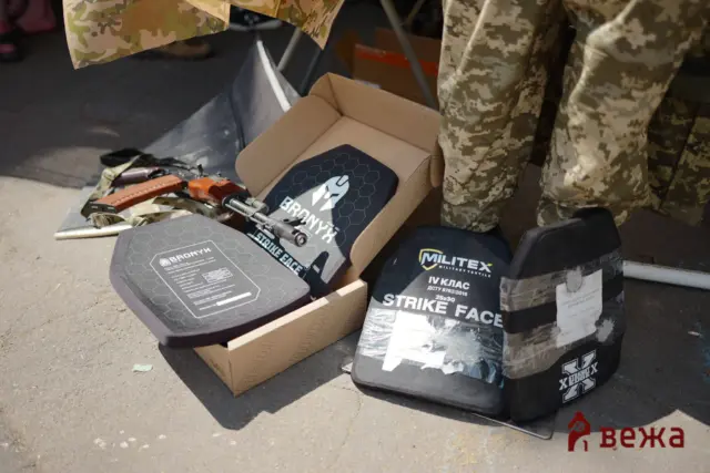 Cardboard box opened to reveal hex-patterned protective face shields labeled 'BRONYX Strike Face' among tactical gear and camouflage pants.