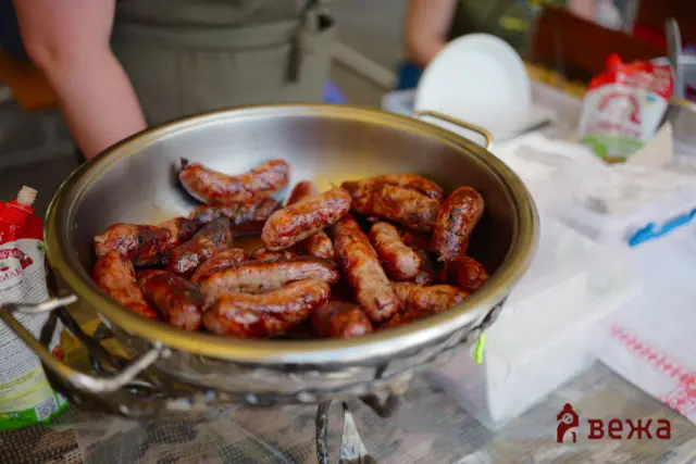 Bowl of grilled sausages resting in a metal pot on a table with cooking supplies nearby