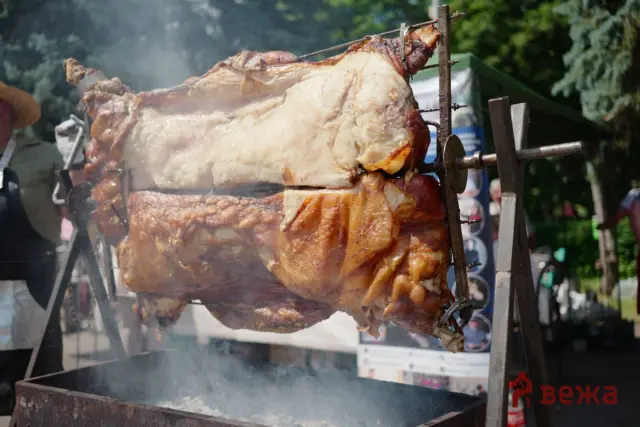 Whole roasted pig on a spit over an open grill, smoke rising at an outdoor barbecue festival