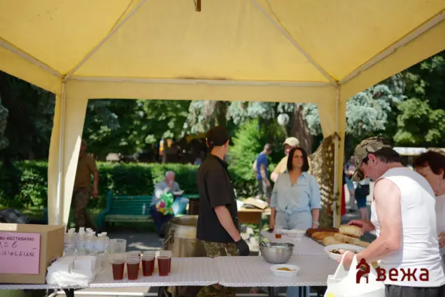 Outdoor festival booth under a yellow canopy serving food and drinks to people nearby.