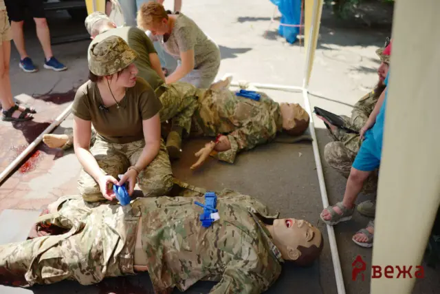 Military personnel in camouflage perform first aid on injured mannequins inside an ambulance during a field medical drill.