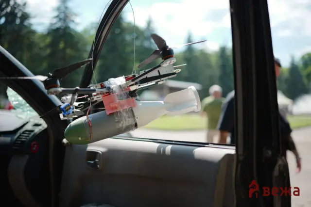 Close-up of a DIY quadcopter mounted on a car dashboard, with exposed wires and propellers, seen through an open window.