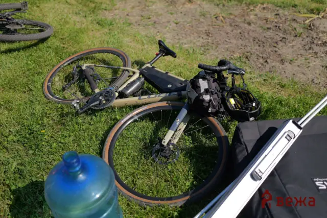 Two mountain bikes lying on grass with a backpack and water bottle nearby.