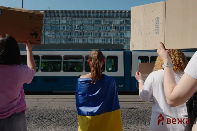 People seen from behind holding up large cardboard boxes on a train platform beside a stationary train.