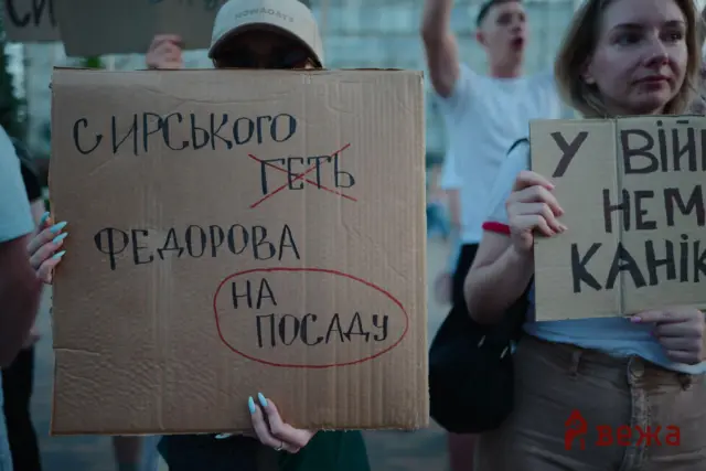 Protest scene with people holding large cardboard signs featuring handwritten Cyrillic text and red markings.