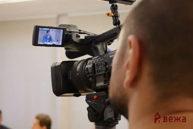 Close-up of a professional video camera recording a man in a blue suit, shown on the camera's LCD display.
