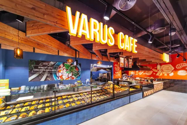 Interior of Varus Café showing a pastry counter with glass display and warm pendant lighting over blue-tiled walls and wooden beams