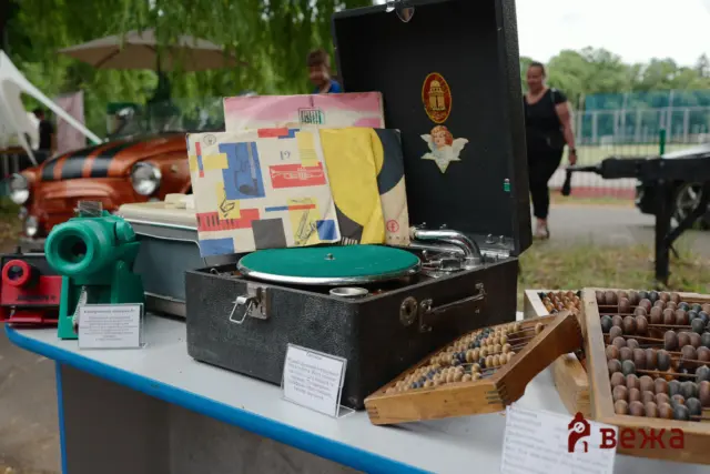 Outdoor market stall showing vintage electronics and abacuses; a black suitcase-like device and a colorful wrapped box on a blue table.