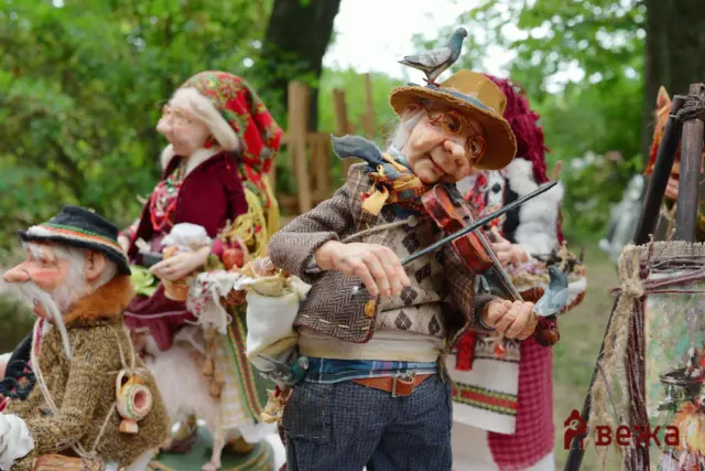 Life-sized rag dolls in vintage clothing performing a violin tune at an outdoor festival.