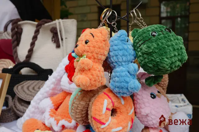 Colorful fuzzy stuffed animal keychains hanging on display, including orange, blue, and green creatures with eyes and chains.