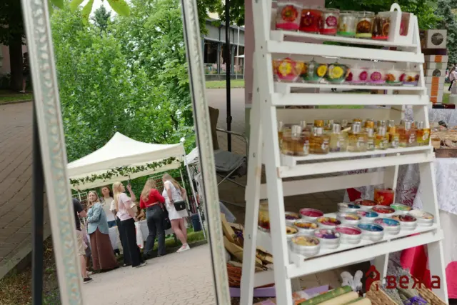 Outdoor market stall with shelves of colorful candles and jars, people chatting in the background.