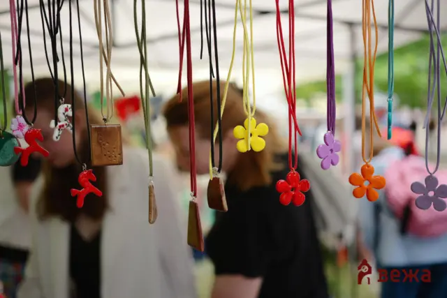 Colorful pendant necklaces and charms hanging from cords at a market stall, with blurred shoppers in the background.