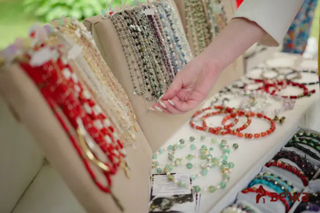 A shopper's hand reaching toward a display of colorful beaded necklaces and bracelets.